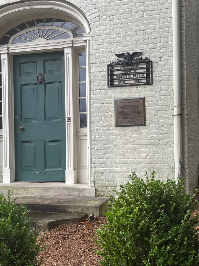 Green entry door at the James K. Polk Home in Columbia with historical plaques displayed beside it.