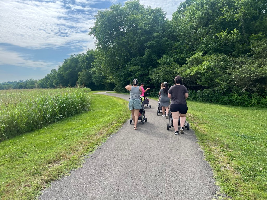 Moms walking with strollers on the paved loop trail at Jerry Erwin Park in Spring Hill Tennessee, with trees on one side and ornamental grass on the other.