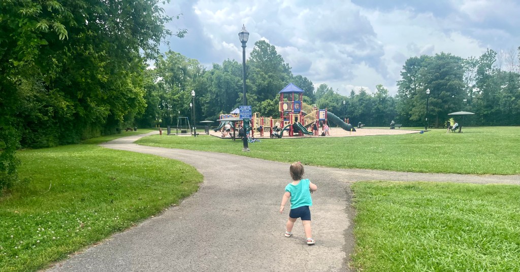 Child running on the paved walking trail at Harvey Park in Spring Hill Tennessee toward the playground surrounded by trees and open green space.